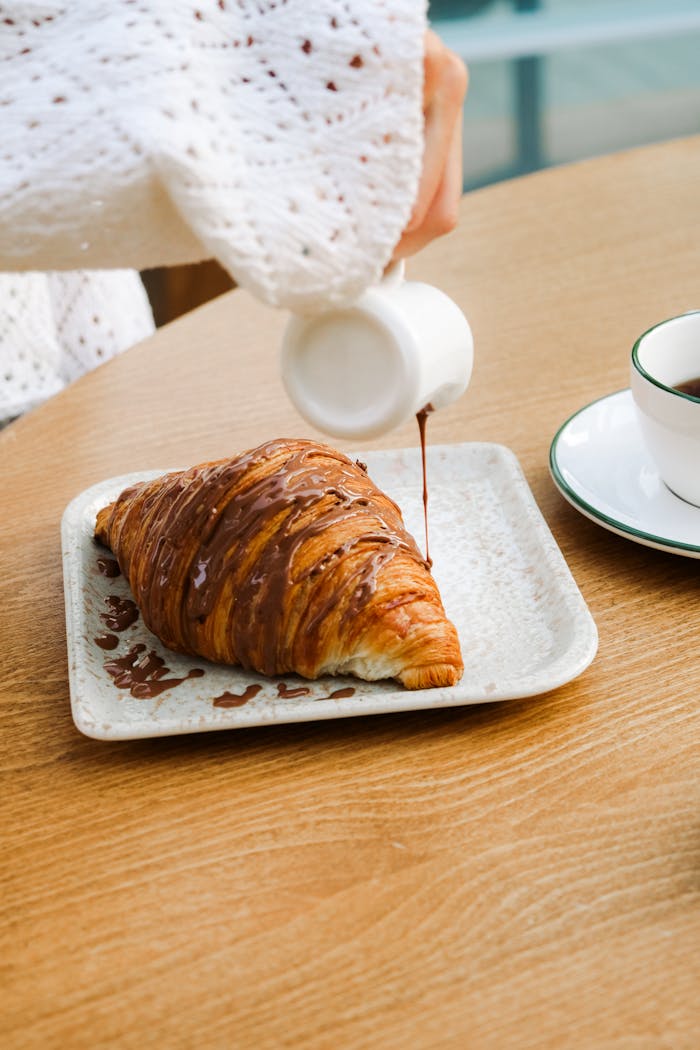 A warm croissant drizzled with chocolate sauce in an Adana café setting.